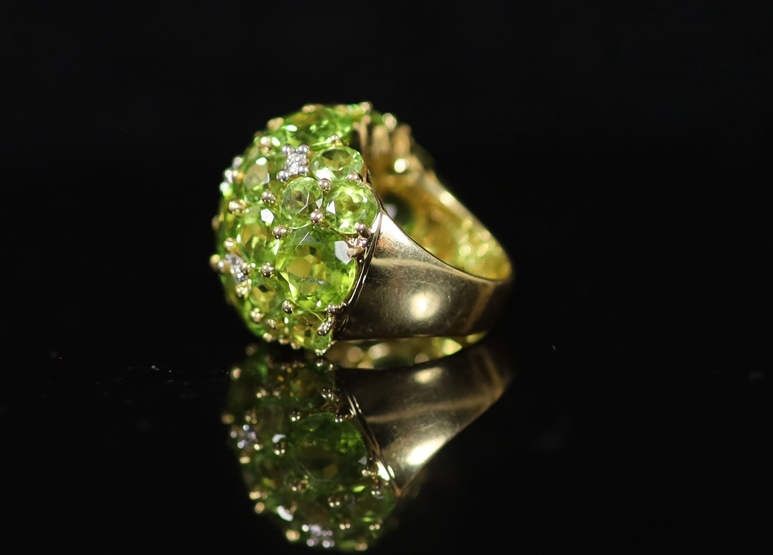 A Continental 18k gold and graduated round cut peridot encrusted dress ring, with diamond chip spacers